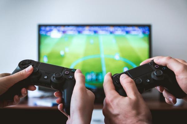 two pairs of hands hands holding games consoles in front of a screen